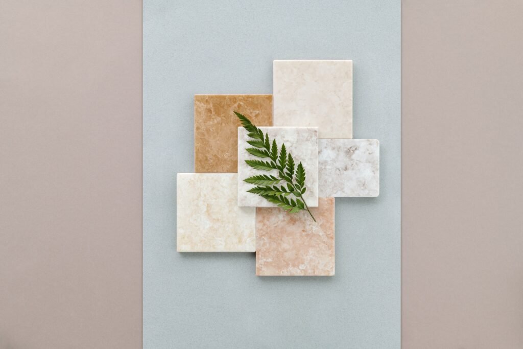 A minimalist flat lay of marble tiles on a gray surface featuring a green fern leaf.